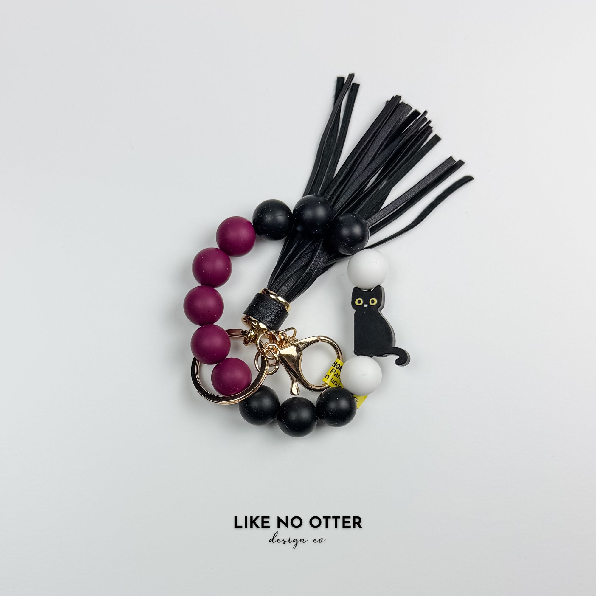 Keychain with black cat charm, beads, and tassels on a light gray background