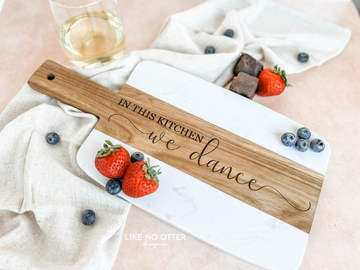 Acacia wood and marble charcuterie or serving board with engraving "in this kitchen we dance" on wood. Engraved and sold by Like No Otter Design Co